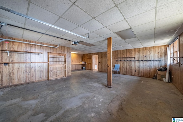 basement featuring a drop ceiling, wooden walls, and a garage