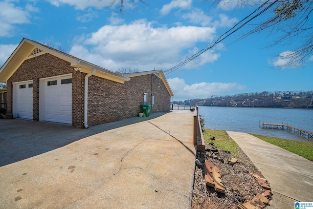 view of side of property with a garage, a water view, brick siding, and driveway