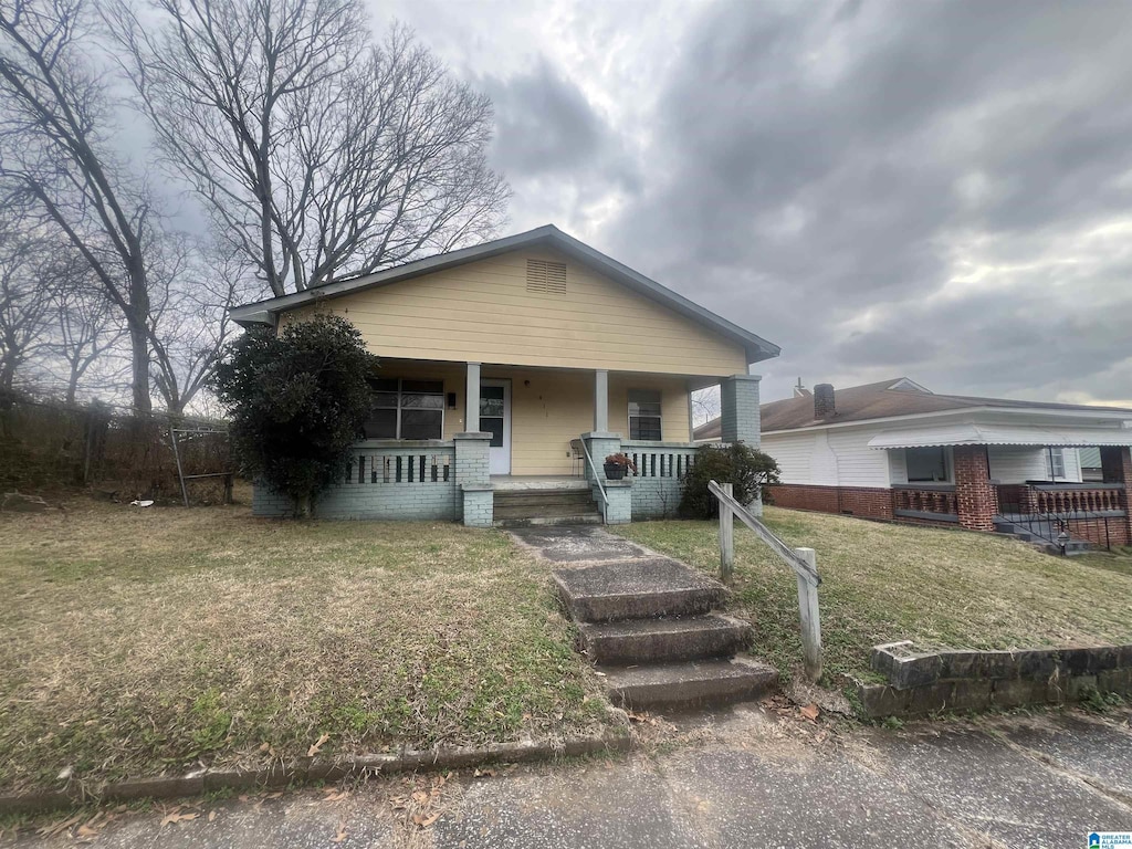 bungalow-style house with brick siding, covered porch, and a front lawn