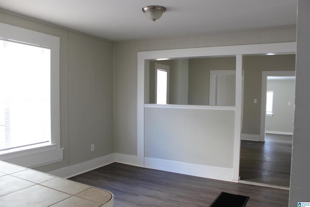 empty room featuring baseboards, dark wood-style flooring, and a wealth of natural light