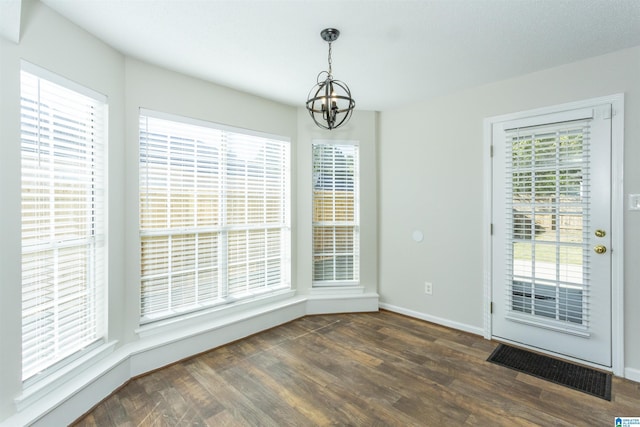 unfurnished dining area with an inviting chandelier, baseboards, and dark wood-type flooring