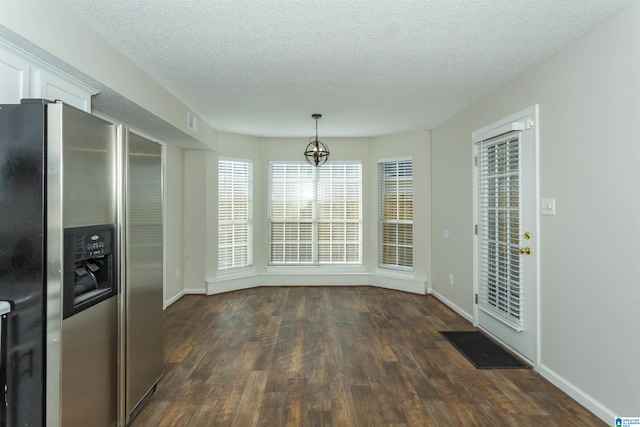 unfurnished dining area with visible vents, baseboards, a notable chandelier, a textured ceiling, and dark wood-style flooring