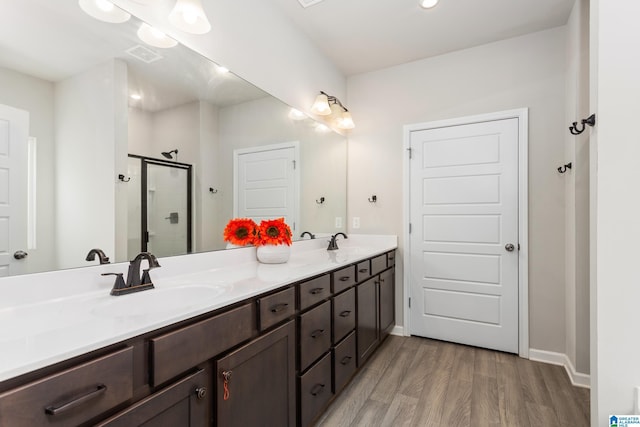 full bath with a shower stall, wood finished floors, double vanity, and a sink