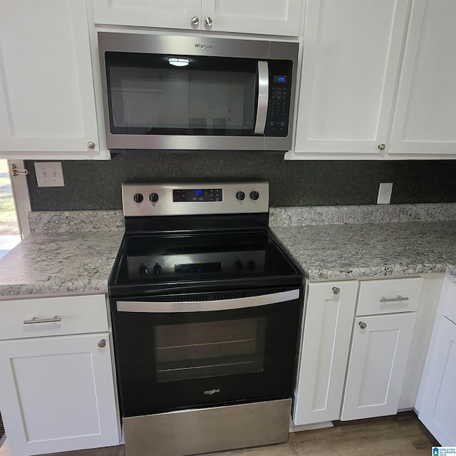 kitchen featuring tasteful backsplash, white cabinetry, stainless steel appliances, and light stone countertops