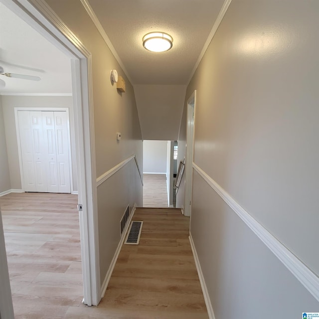 hall with an upstairs landing, light wood-style floors, and ornamental molding