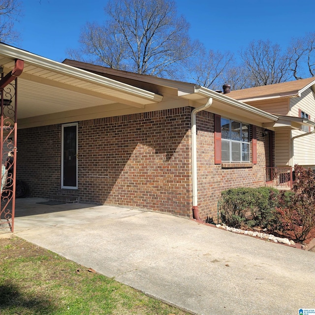 view of side of property with brick siding, an attached carport, and concrete driveway