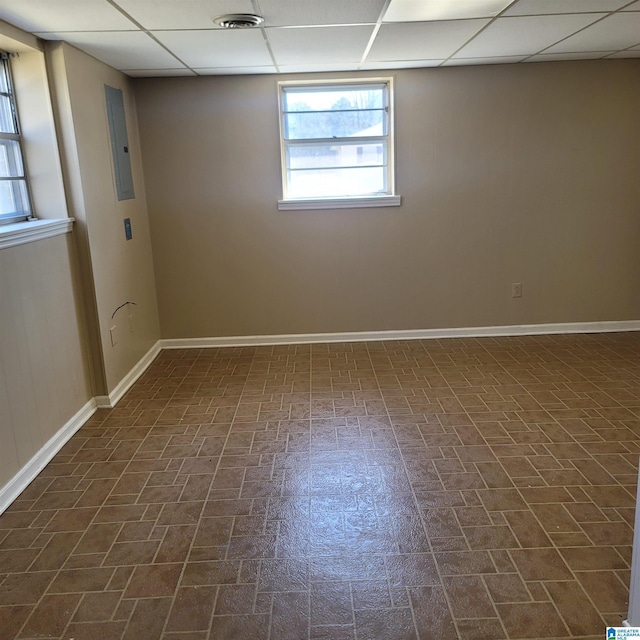 unfurnished room with brick patterned floor, electric panel, baseboards, and a drop ceiling