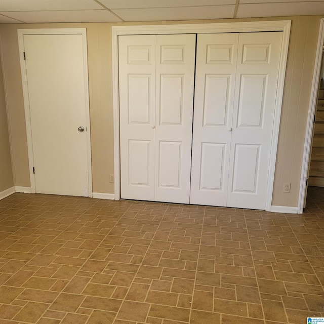 unfurnished bedroom with a drop ceiling, a closet, baseboards, and brick patterned floor