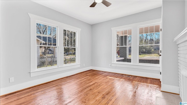 unfurnished room featuring baseboards, wood finished floors, ceiling fan, and a fireplace