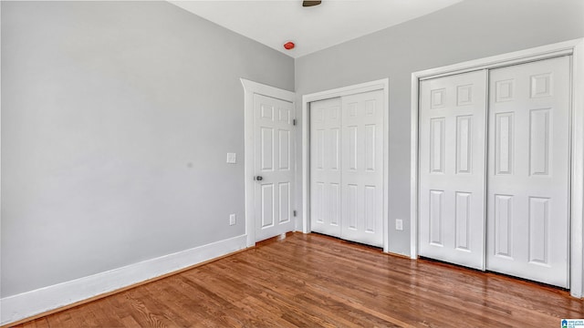 unfurnished bedroom featuring wood finished floors, multiple closets, and baseboards