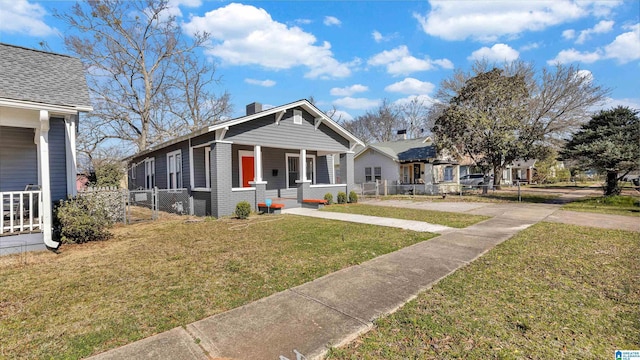 bungalow with a front lawn, a porch, fence, brick siding, and a chimney