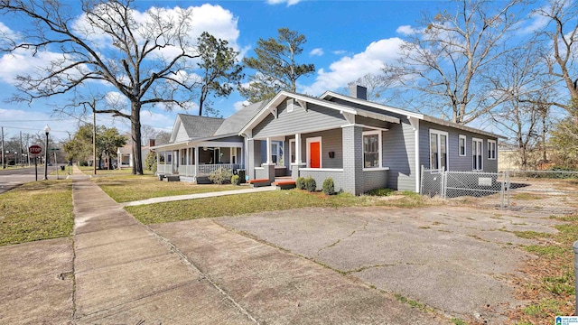 view of front facade with a front yard, fence, covered porch, a chimney, and brick siding