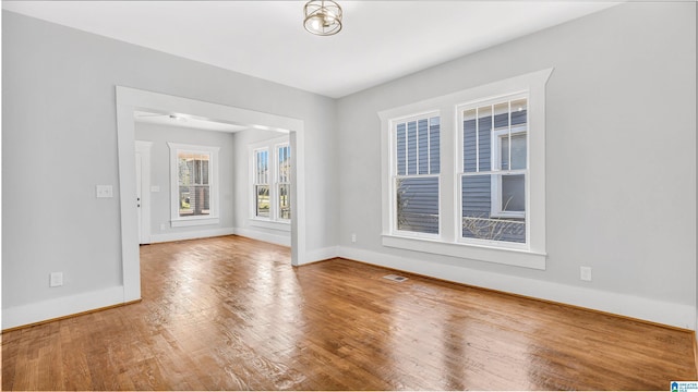 empty room with wood finished floors, visible vents, and baseboards