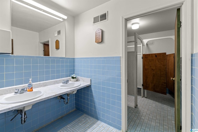 bathroom with tile walls, visible vents, tile patterned floors, and a sink