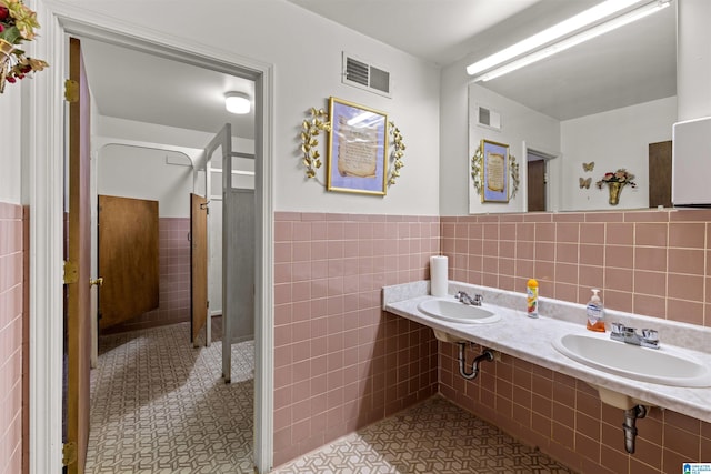 bathroom with a wainscoted wall, tile walls, visible vents, and a sink