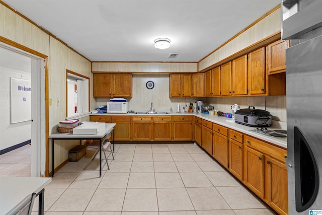 kitchen with light tile patterned floors, white microwave, freestanding refrigerator, light countertops, and brown cabinets