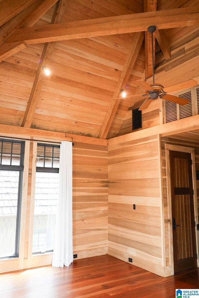 unfurnished room with wood finished floors, lofted ceiling with beams, ceiling fan, wood walls, and wooden ceiling