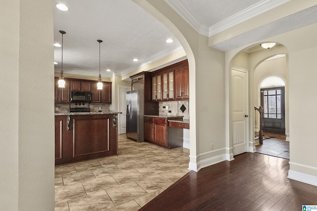 kitchen featuring stainless steel refrigerator with ice dispenser, arched walkways, black microwave, decorative backsplash, and light stone countertops