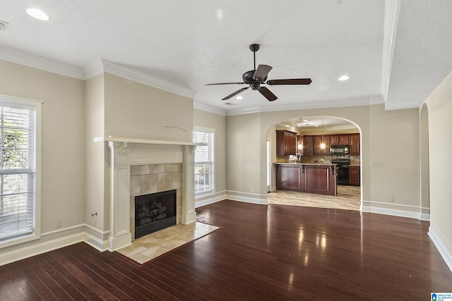 unfurnished living room featuring baseboards, arched walkways, light wood-style floors, and crown molding