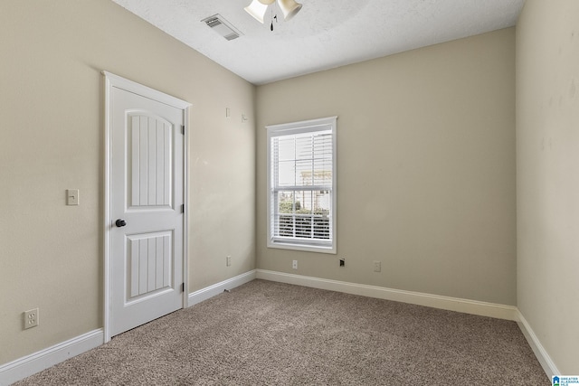 unfurnished room with carpet flooring, baseboards, visible vents, and a textured ceiling