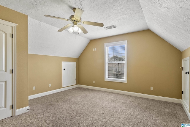 additional living space with visible vents, a textured ceiling, lofted ceiling, and a ceiling fan