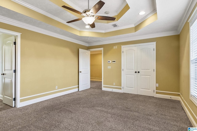 unfurnished bedroom with visible vents, ornamental molding, a tray ceiling, a closet, and carpet floors