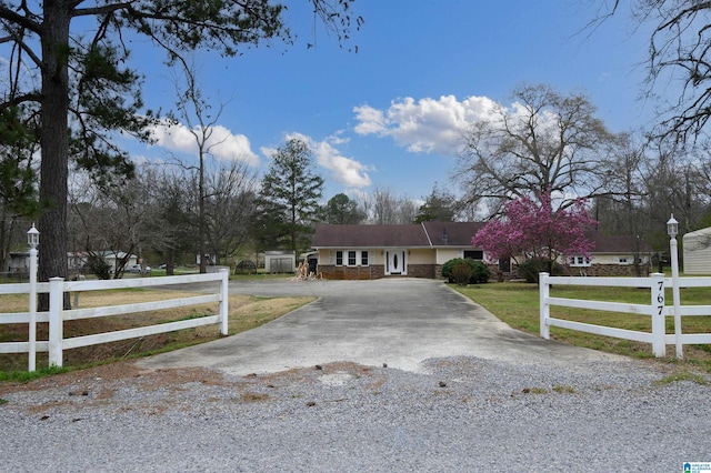 ranch-style home with a fenced front yard, stone siding, a front yard, and driveway