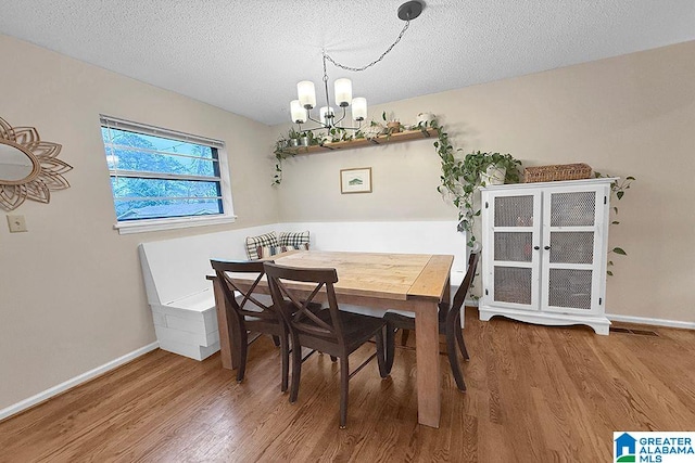 dining space featuring baseboards, a textured ceiling, an inviting chandelier, and wood finished floors