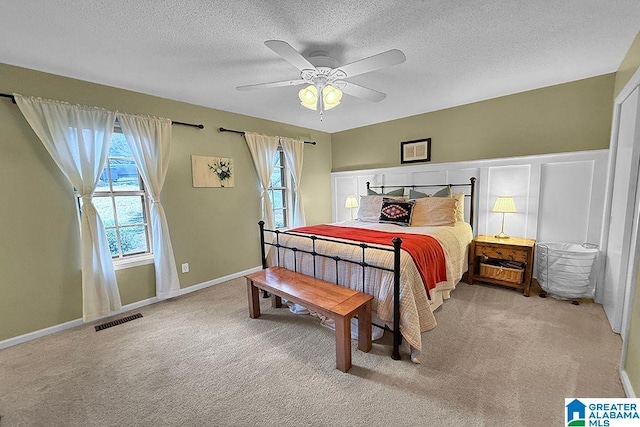 carpeted bedroom with visible vents, a textured ceiling, wainscoting, and a ceiling fan