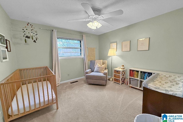 bedroom featuring visible vents, a crib, baseboards, carpet floors, and a textured ceiling