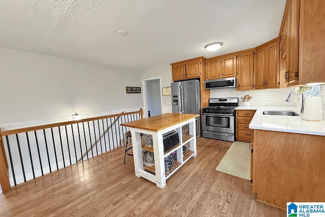 kitchen featuring light wood finished floors, a sink, light countertops, appliances with stainless steel finishes, and backsplash