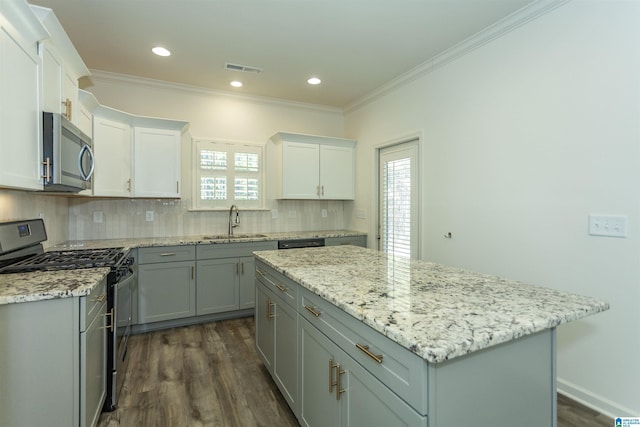 kitchen featuring a sink, a center island, appliances with stainless steel finishes, crown molding, and decorative backsplash