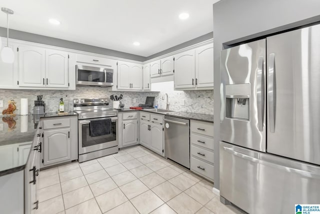 kitchen with light tile patterned floors, a sink, decorative backsplash, appliances with stainless steel finishes, and white cabinetry