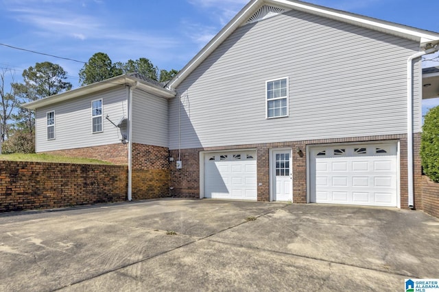 view of property exterior with brick siding, a garage, and driveway