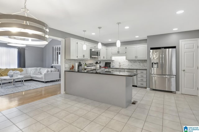 kitchen featuring appliances with stainless steel finishes, white cabinetry, dark countertops, open floor plan, and backsplash