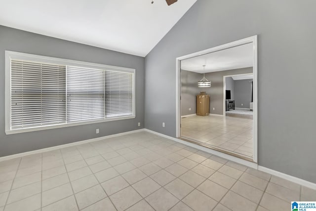 tiled empty room with vaulted ceiling, a ceiling fan, and baseboards