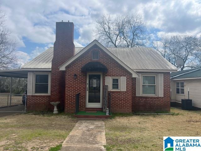 view of front of house featuring metal roof, brick siding, central AC, and fence