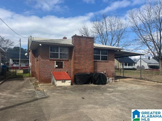 back of property featuring brick siding, metal roof, a chimney, and a carport