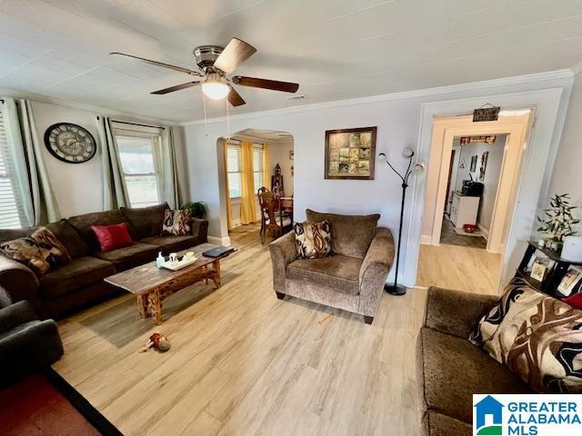 living room featuring arched walkways, light wood-style floors, ceiling fan, and crown molding