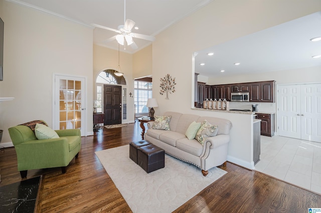 living area featuring a ceiling fan, wood finished floors, crown molding, baseboards, and a towering ceiling