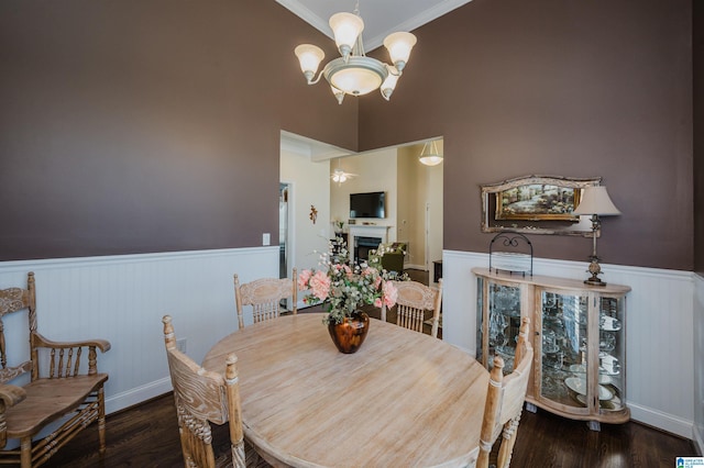 dining area with a fireplace, wood finished floors, a wainscoted wall, and a chandelier