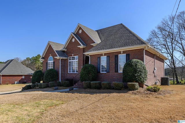 view of front of home featuring brick siding, central AC unit, a front lawn, and a shingled roof