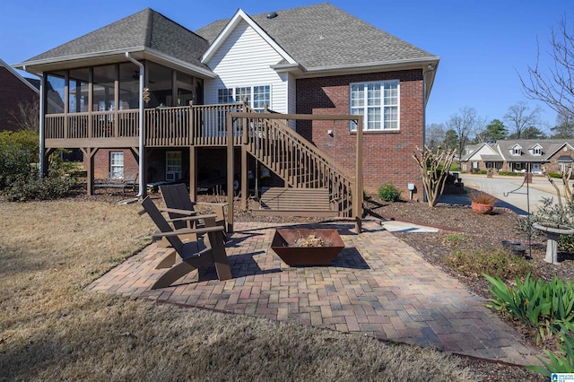 rear view of property featuring brick siding, a fire pit, stairway, a sunroom, and a patio area