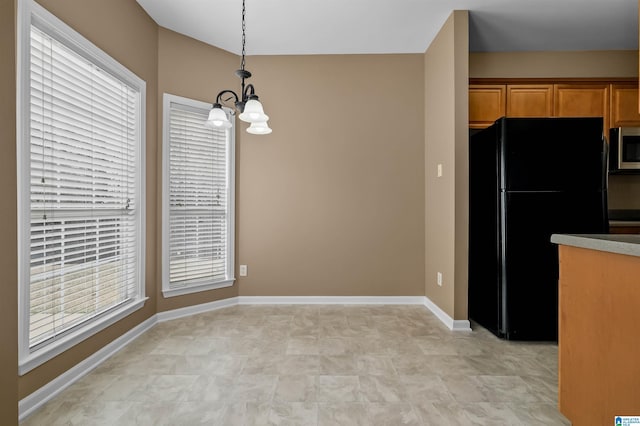 kitchen with stainless steel microwave, baseboards, freestanding refrigerator, an inviting chandelier, and hanging light fixtures