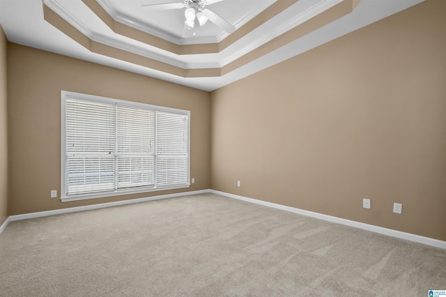 empty room featuring a raised ceiling, carpet, a ceiling fan, and crown molding