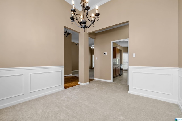 spare room with a chandelier, carpet flooring, wainscoting, and a decorative wall