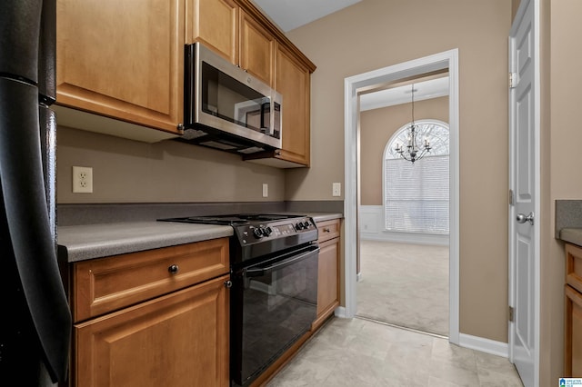 kitchen featuring a wainscoted wall, an inviting chandelier, black appliances, light colored carpet, and brown cabinets