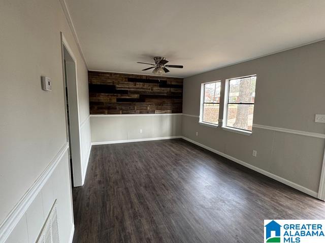 unfurnished room with wooden walls, baseboards, dark wood-type flooring, and ceiling fan