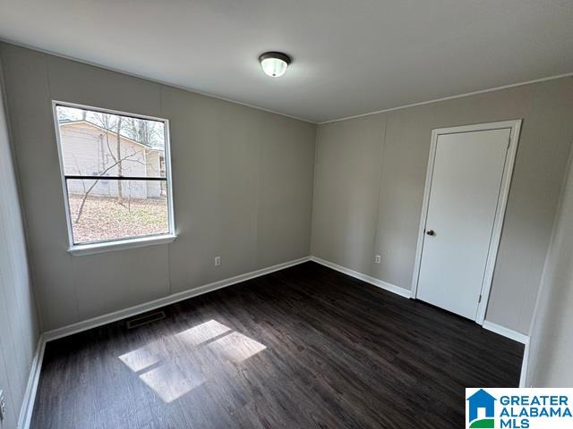 unfurnished room with visible vents, baseboards, and dark wood-style floors