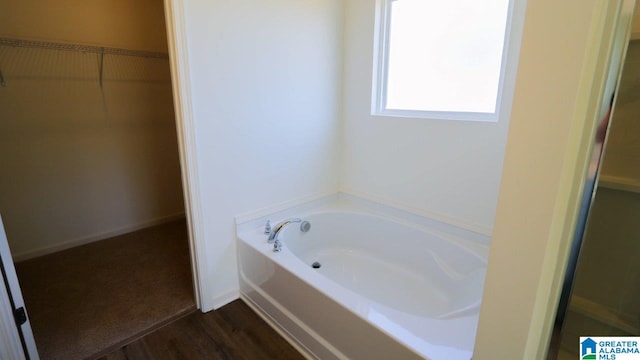 bathroom with a garden tub, a spacious closet, and wood finished floors